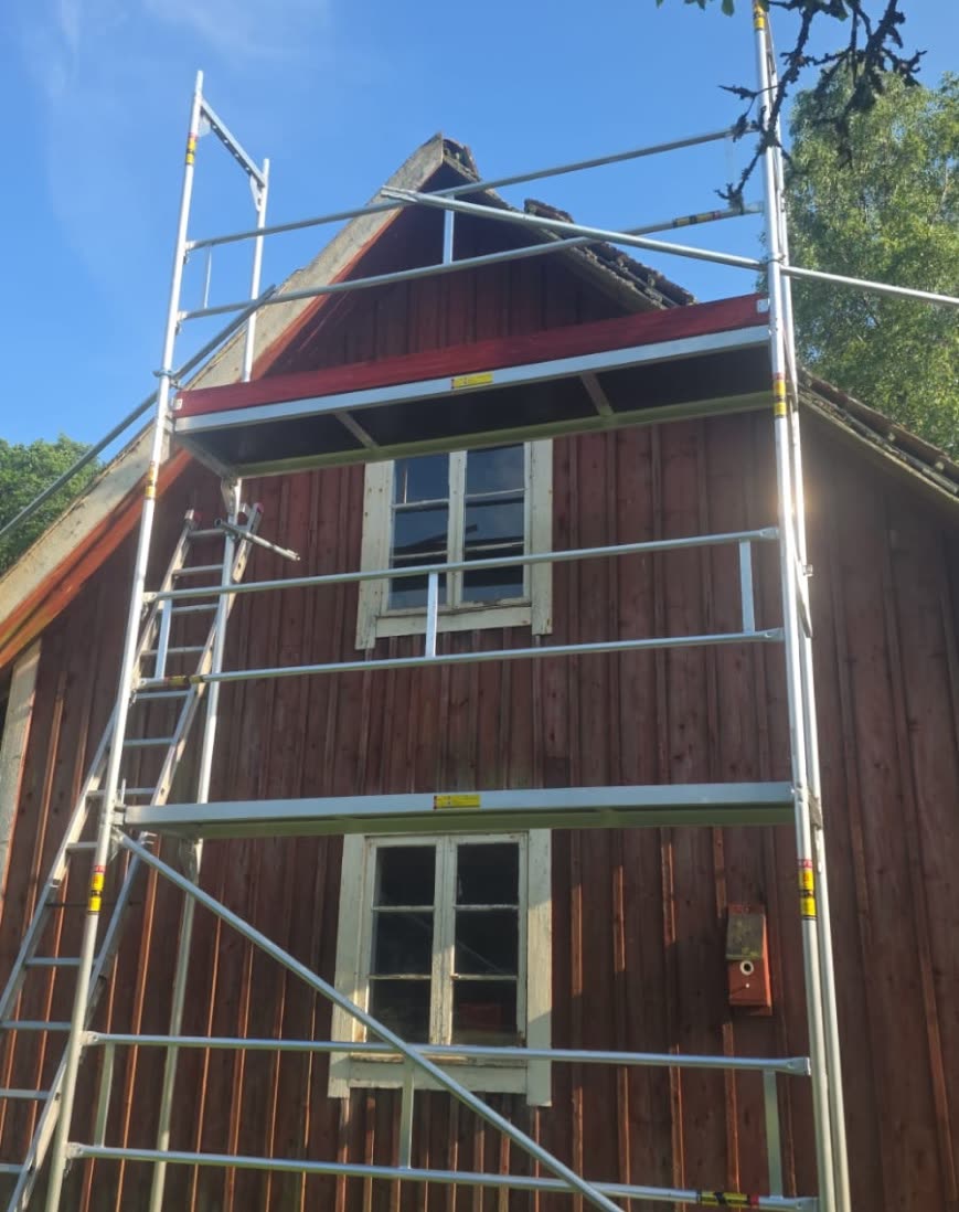 Ställning med stege rest mot gaveln på ett rödmålat trähus