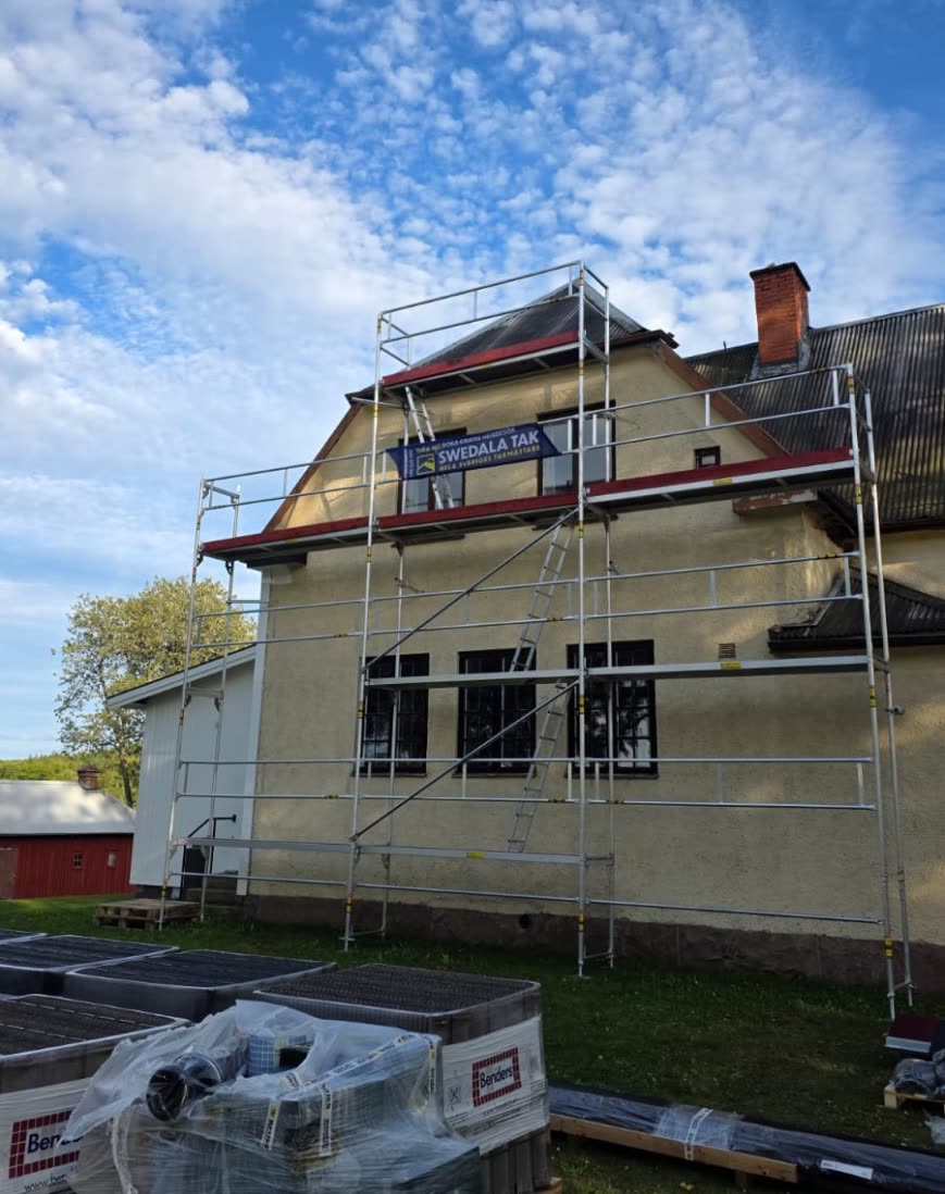 Fasadställning uppsatt längs gaveln på ett putsat bostadshus inför takarbete