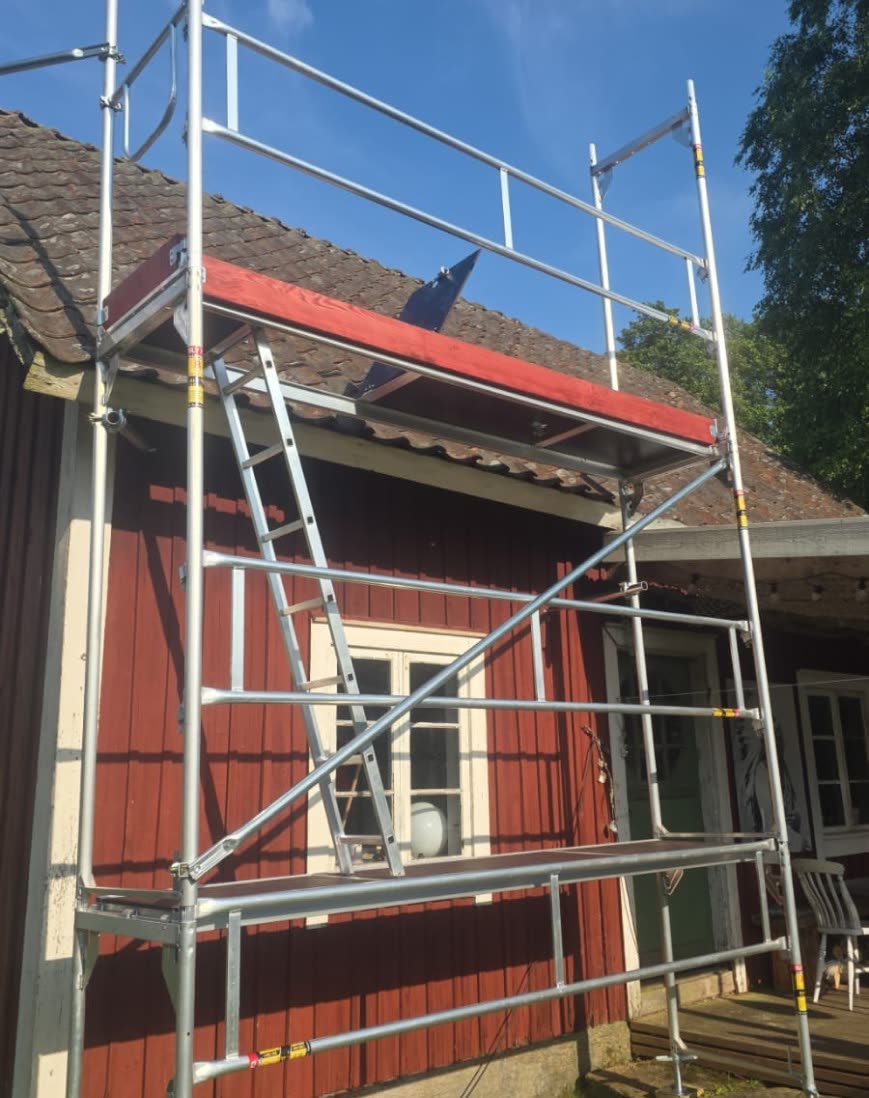 Ställning med invändig stege rest mot takfoten på ett rött trähus